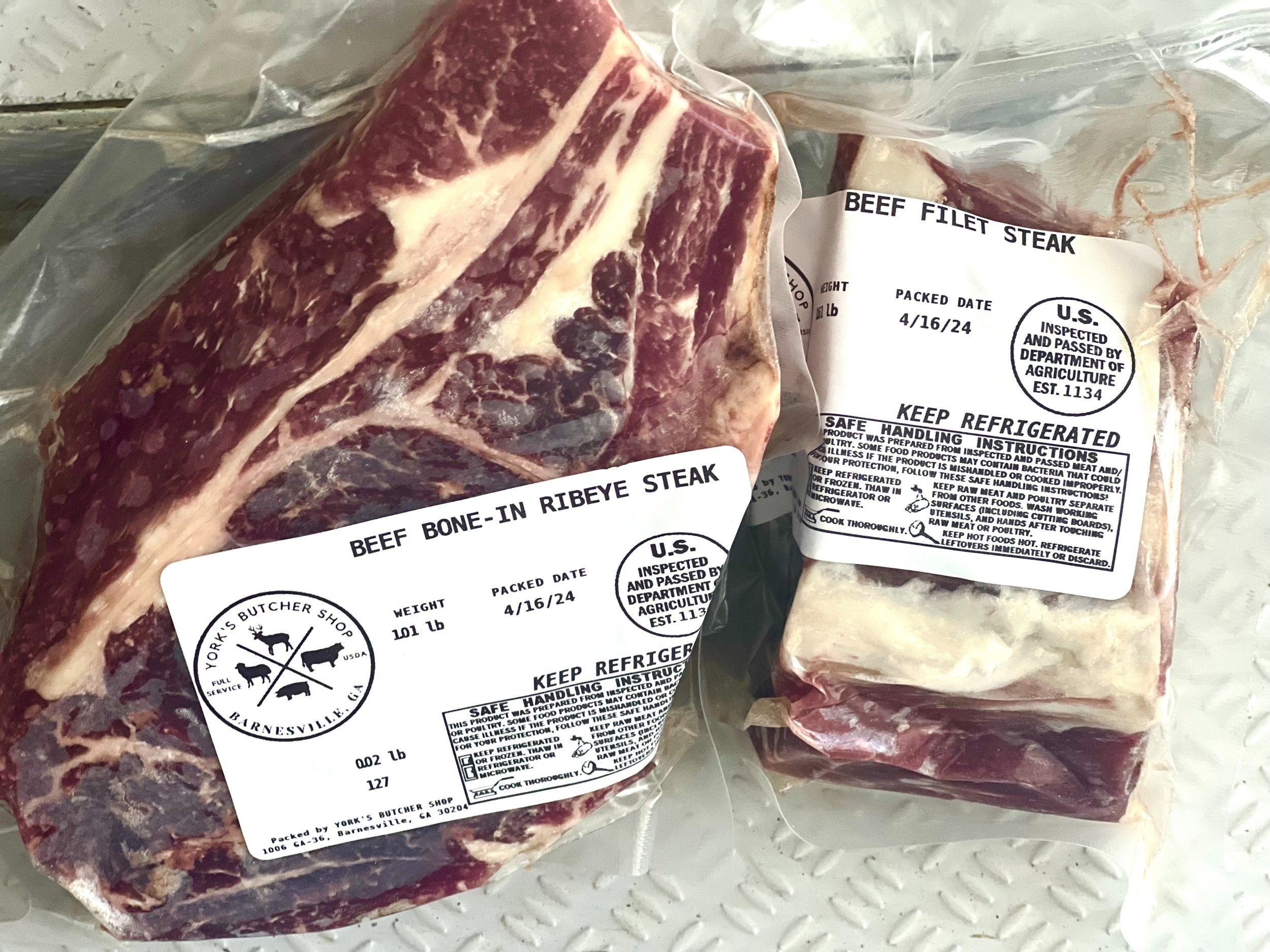 Fresh beef cuts including a bone-in ribeye steak and a filet steak, both labeled with weight and packing date, from York's Butcher Shop in Barnesville, GA.